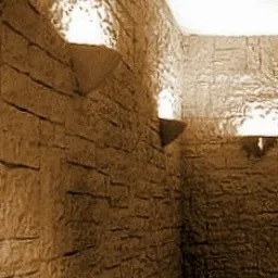 Wnętrze łazienki wykończone płytkami imitującymi kamień w ciepłej, brązowej tonacji. Na ścianach zamontowane trójkątne półki z wbudowanym oświetleniem punktowym, tworzące nastrojowy klimat.